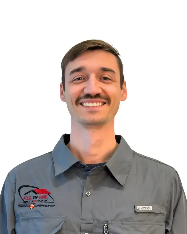 A man with short brown hair and a mustache smiles at the camera. He wears a gray collared work shirt with embroidered logos and a name tag. The background is plain white.