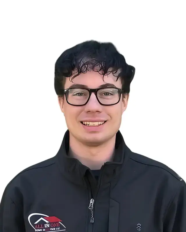 A young man with short, curly dark hair and glasses smiles at the camera. He is wearing a black jacket with a red and white ALL IN ONE logo on the chest, against a white background.